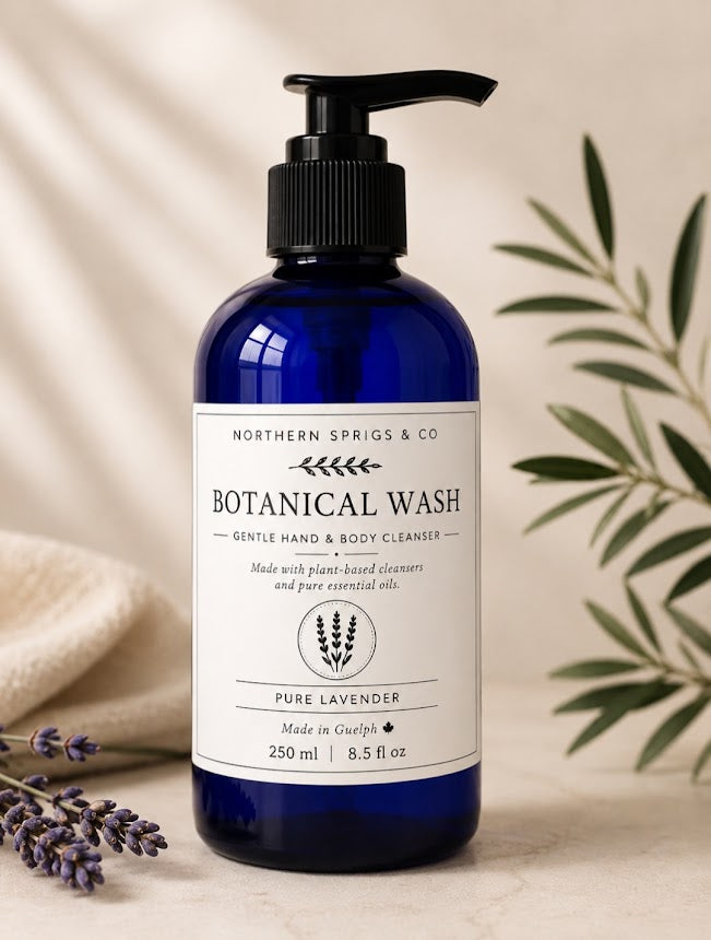 A bottle of Northern Springs & Co Botanical Wash Pure Lavender hand and body cleaner, in a deep cobalt blue bottle with a black pump and white label, styled with lavender sprigs and olive leaves on a neutral beige background.